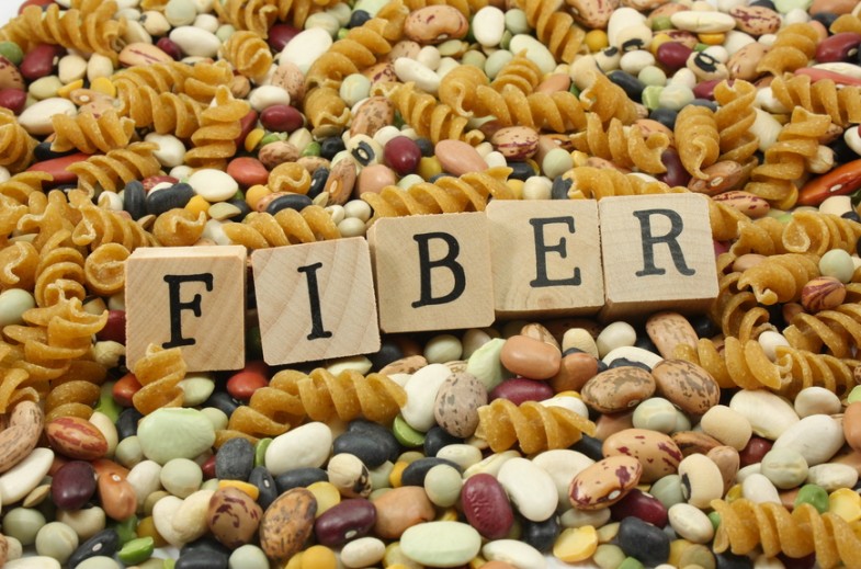 Wooden blocks spelling out the word FIBER photographed with a background of high fiber foods.